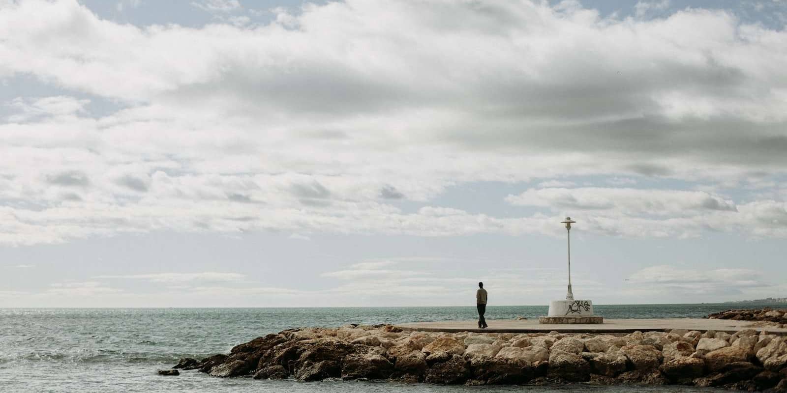 person standing on brown rock formation near body of water under white clouds during daytime